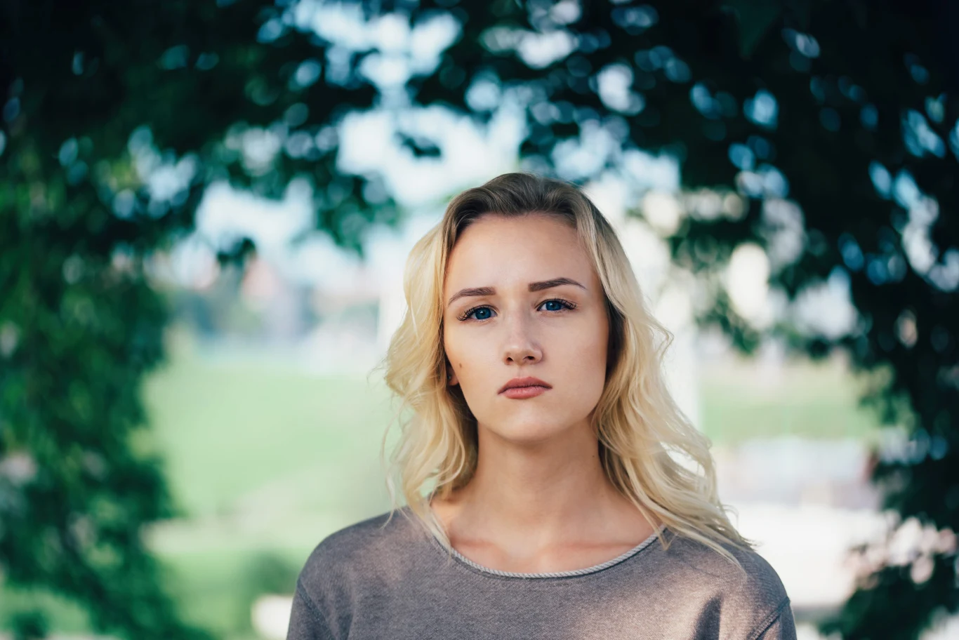 Życie bez dramy ich nie interesuje. Oto najbardziej emocjonalne znaki zodiaku Młoda kobieta o blond włosach i jasnej cerze w szarej bluzce, stoi pośród zieleni drzew, patrzy przed siebie