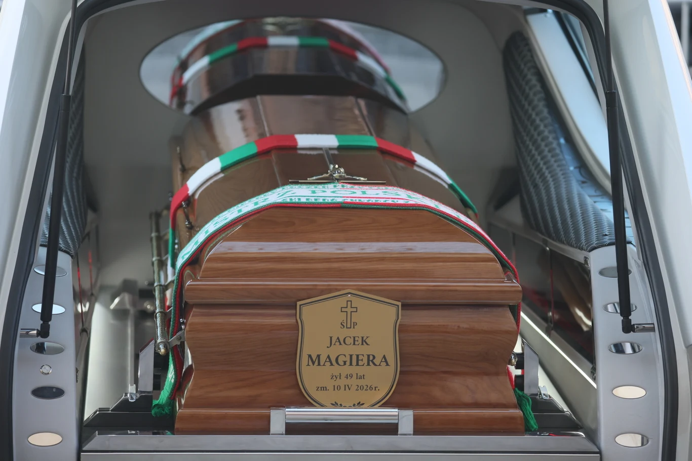 Pogrzeb Jacka Magiery drewniana trumna z tabliczką, na której widnieje imię i nazwisko Jacek Magiera, umieszczona w tylnej części karawanu, ozdobiona biało-czerwono-zieloną wstęgą