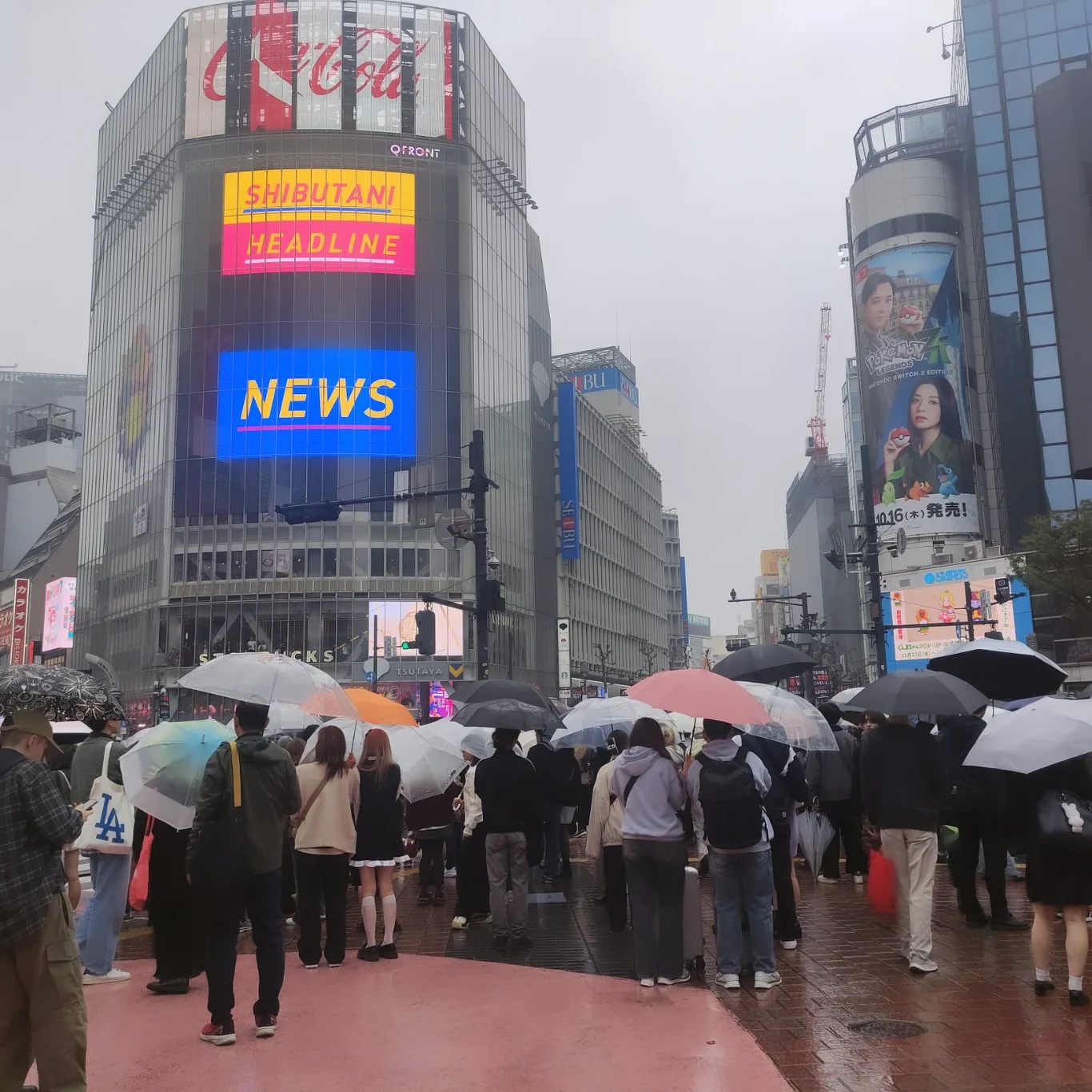 O tłum w Japonii nie trudno tłum ludzi z parasolami przechodzących przez słynne skrzyżowanie w centrum Tokio, na tle wysokich budynków z dużymi, kolorowymi ekranami reklamowymi
