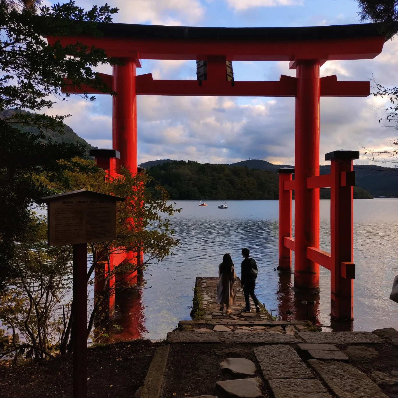 Japonia była moim podróżniczym marzeniem duża czerwona brama torii nad wodą, u stóp której stoi troje ludzi, w tle spokojne jezioro otoczone zielonymi wzgórzami i łodzie na tafli wody