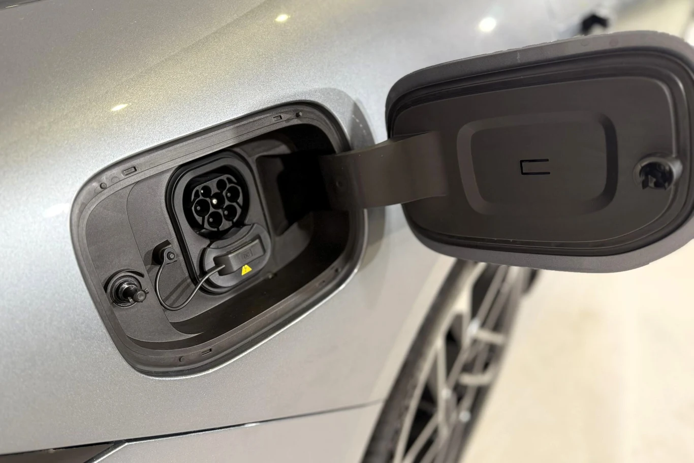 gniazdo ładowania samochodu elektrycznego z otwartą klapką, widoczne złącze typu Plug-In oraz fragment srebrnej karoserii i koła pojazdu