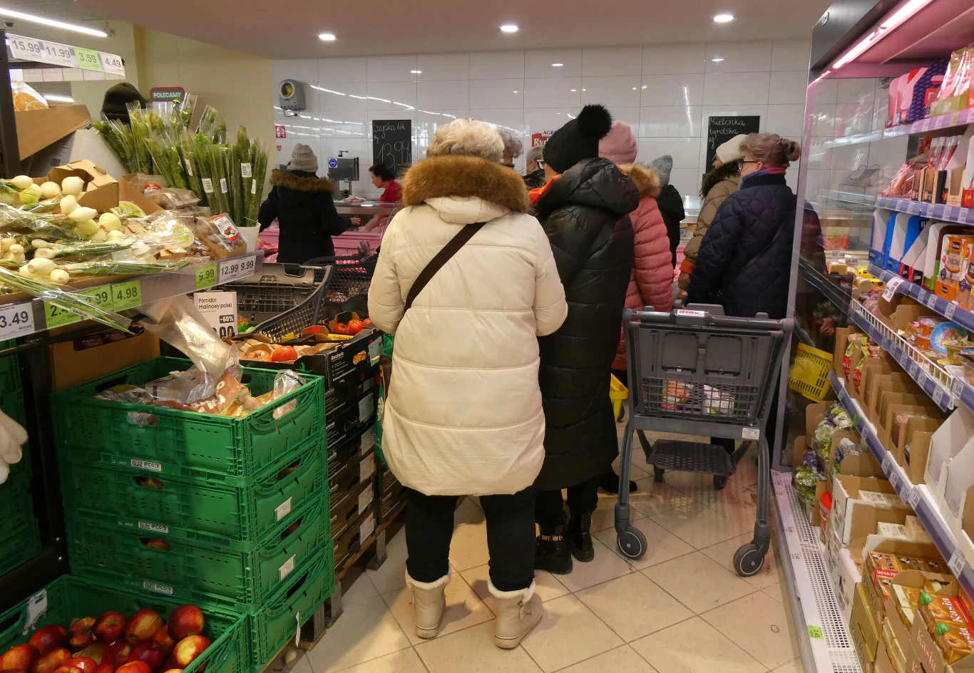 Zakończyły się kontrole w Dino. Stwierdzono nieprawidłowości Klienci w zimowych kurtkach stojący w kolejce przy kasie w sklepie Dino, otoczeni półkami z produktami.