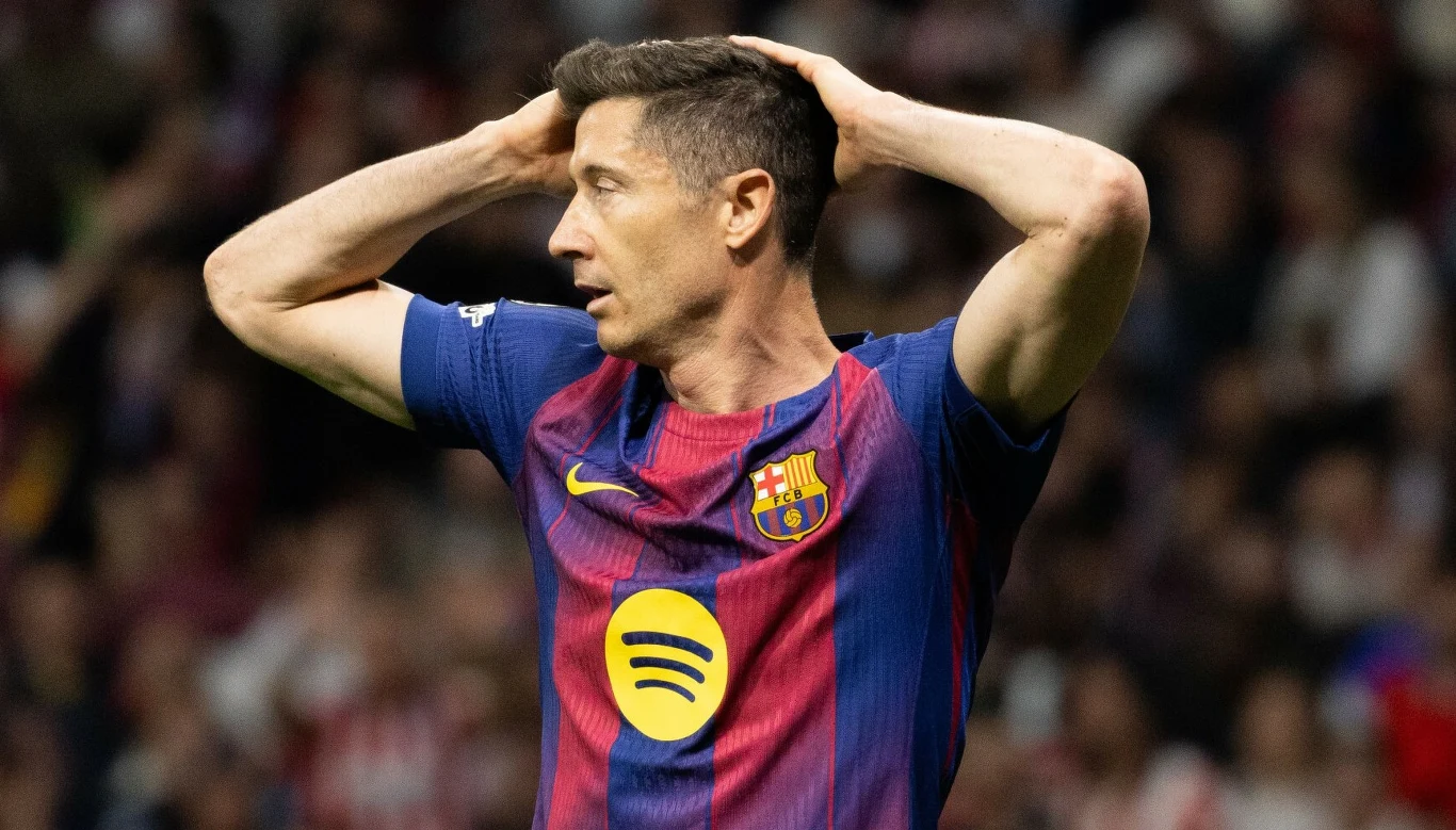 Robert Lewandowski piłkarz FC Barcelony w granatowo-bordowej koszulce, trzyma ręce na głowie w geście rozczarowania, na tle rozmytego stadionu