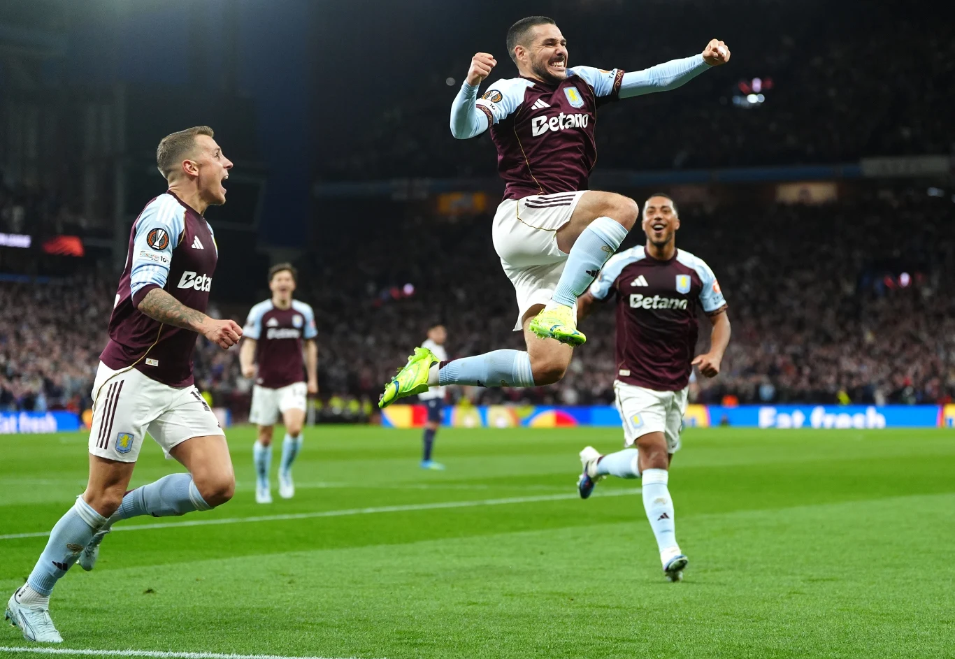Kadr z meczu Aston Villa - Bologna Piłkarz Aston Villi w bordowo-niebieskim stroju skacze, świętując bramkę z drużyną podczas meczu z Bologną.