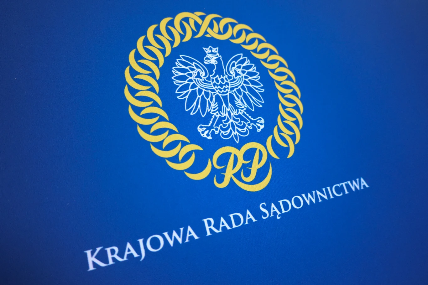 Kryzys sądownictwa nie polega jedynie na brakach kadrowych. Biały orzeł w koronie na niebieskim tle, otoczony złotym wieńcem i napis 'Krajowa Rada Sądownictwa'