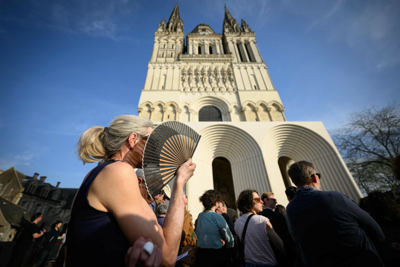 Kontrowersje wokół remontu katedry w Angers. Nie wsztstkim podoba się pomysł japońskiego architekta Kengo Kumy Kobieta z jasnymi włosami i wachlarzem stoi wśród tłumu przed katedrą w Angers na tle jasnego nieba