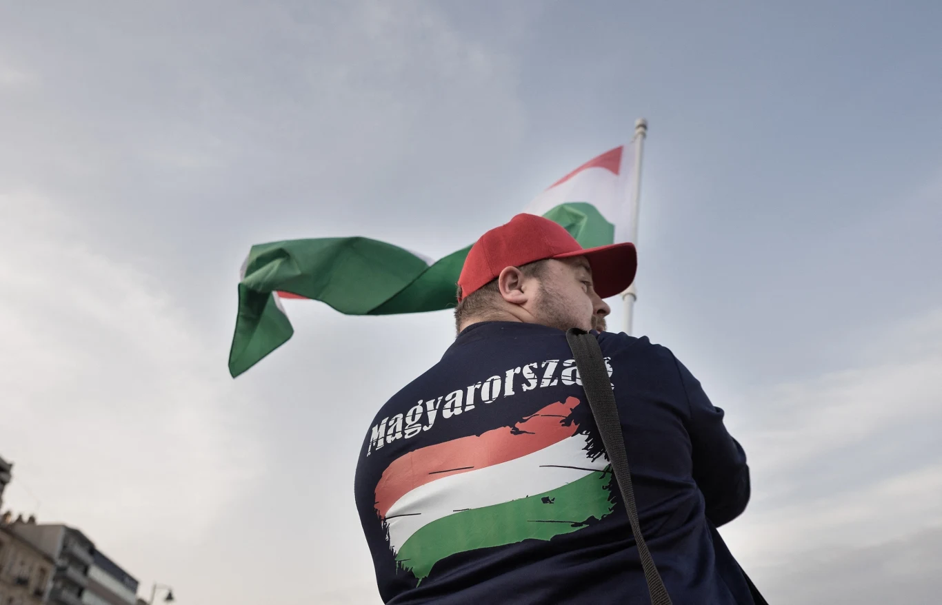 Czy TISZA wprowadzi Węgry do strefy euro? Pierwsze zapowiedzi już słychać. Zdj. ilustracyjne Mężczyzna w czerwonej czapce, granatowej bluzie z napisem 'Magyarország', trzyma flagę Węgier na tle nieba.