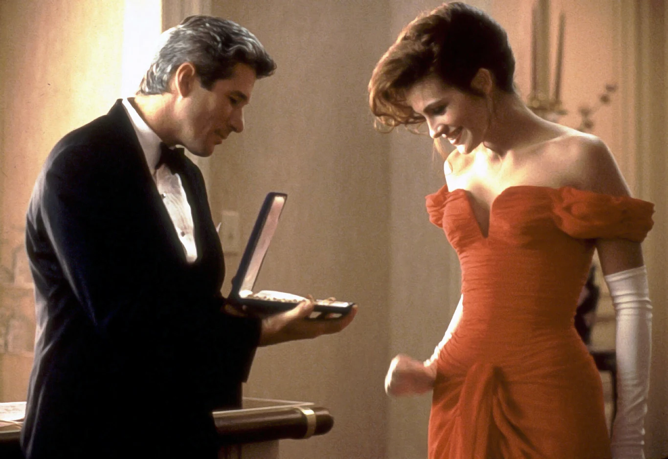 "Pretty Woman" Scena z filmu "Pretty Woman": mężczyzna w smokingu wręcza kobiecie w czerwonej sukni pudełko z biżuterią