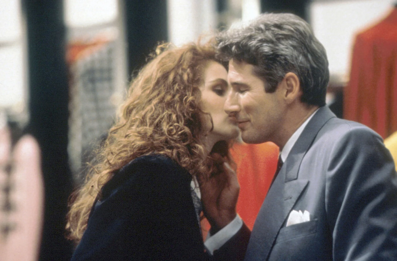 "Pretty Woman" kobieta o długich, kręconych rudych włosach szepcze coś do ucha mężczyźnie w eleganckim garniturze, oboje blisko siebie, ich twarze wyrażają bliskość i zaufanie