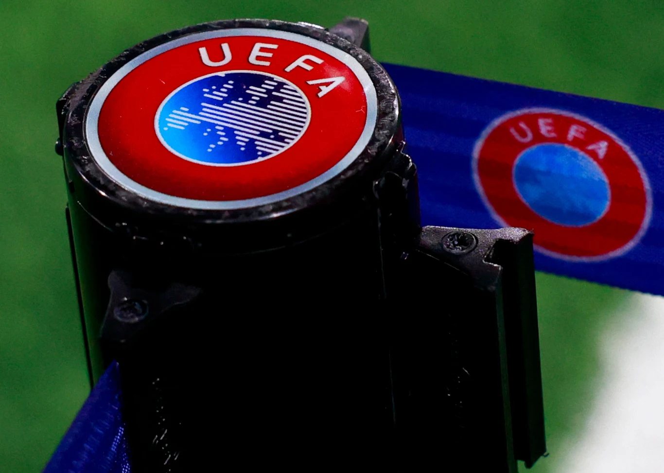 Logo UEFA logo UEFA na czarnym słupku z niebieską taśmą zabezpieczającą, tło rozmyte w kolorze zielonym