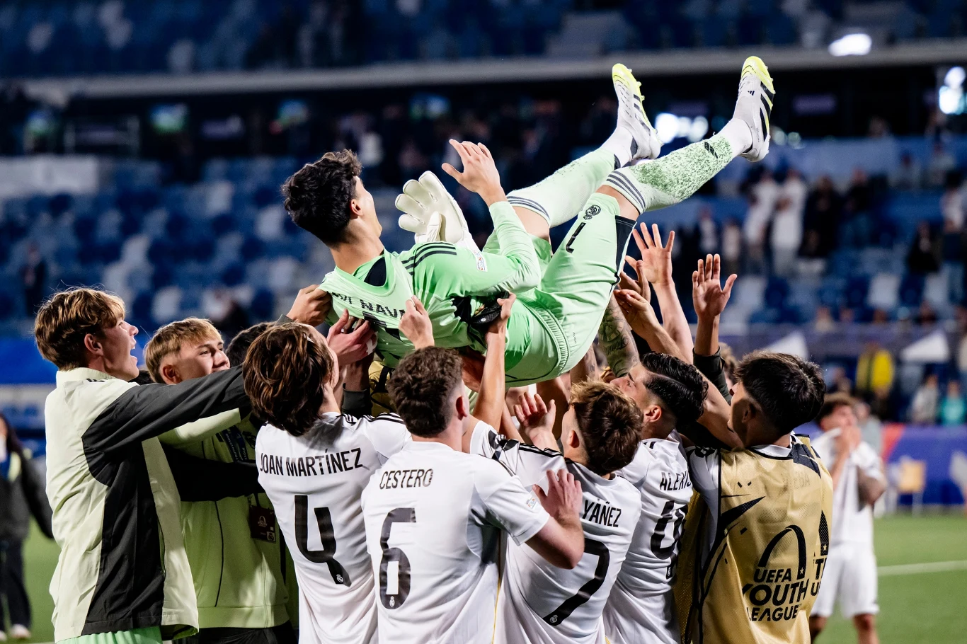 Real Madryt - PSG w młodzieżowej LM grupa młodych piłkarzy w białych strojach rzuca w górę swojego bramkarza w zielonym stroju jako formę świętowania, wokół nich stadion z niebieskimi i białymi trybunami