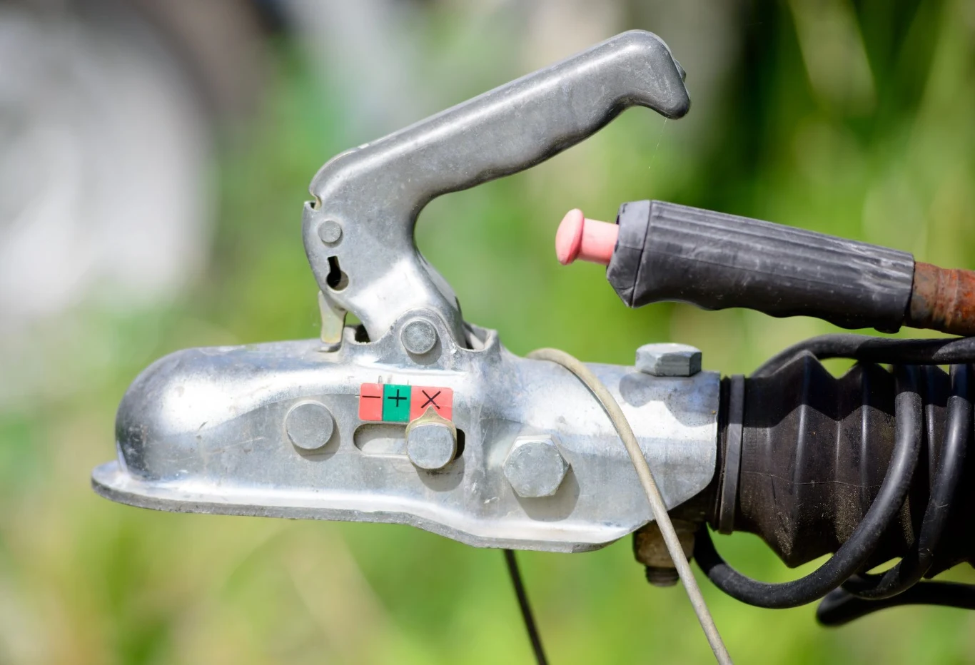 Upadłość Erich Jaeger. Lider branży motoryzacyjnej w kryzysie. Mechanizm zaczepu przyczepy z metalową dźwignią, czarną osłoną i oznaczeniem plus/minus na naklejce