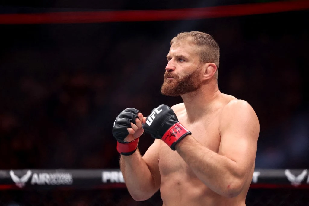 zawodnik MMA w oktagonie w pozycji gotowości do walki, skupiony wyraz twarzy, rękawice ochronne UFC na dłoniach, napięte mięśnie ramion i torsu, w tle rozmyte światła areny