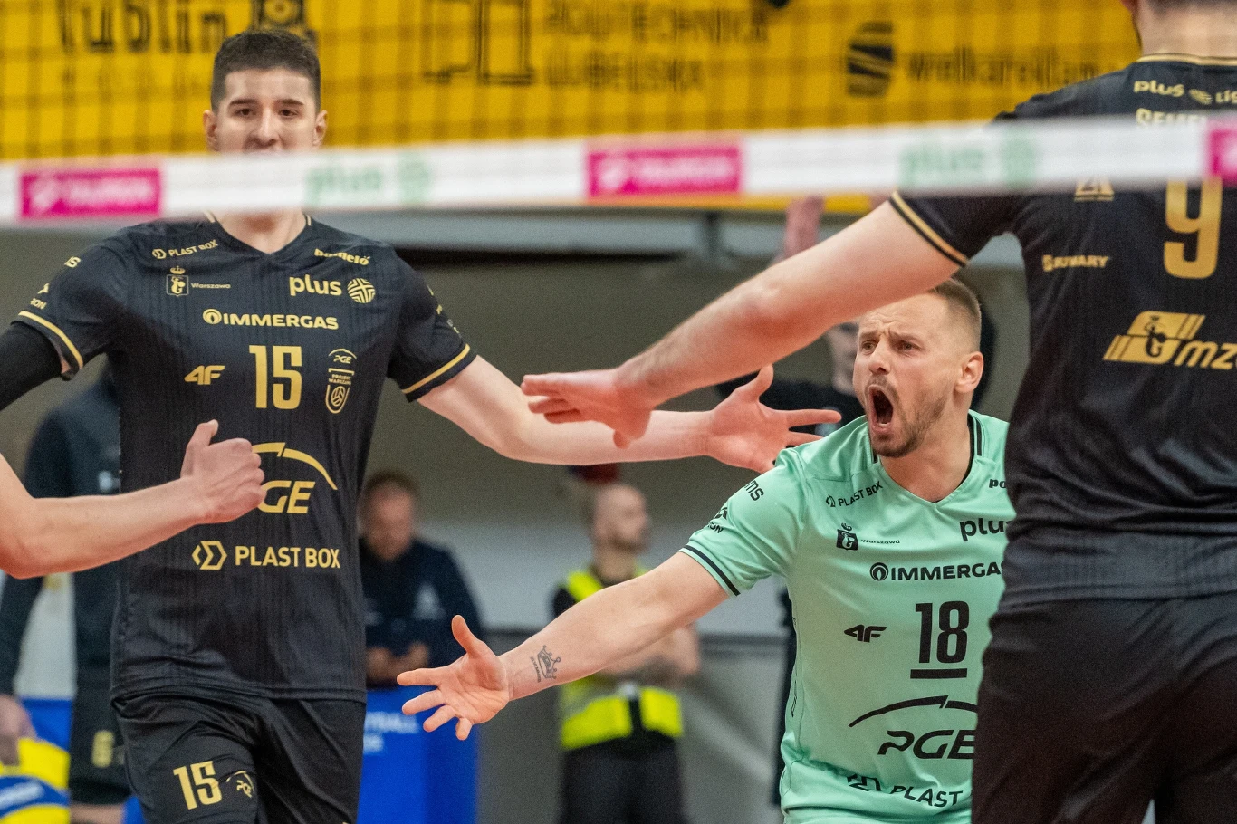 Siatkarze PGE Projektu Warszawa siatkarze drużyny PGE Skra Bełchatów w emocjonującym momencie meczu, jeden zawodnik w zielonej koszulce energicznie gestykuluje, pozostali skupieni i gotowi do kolejnej akcji