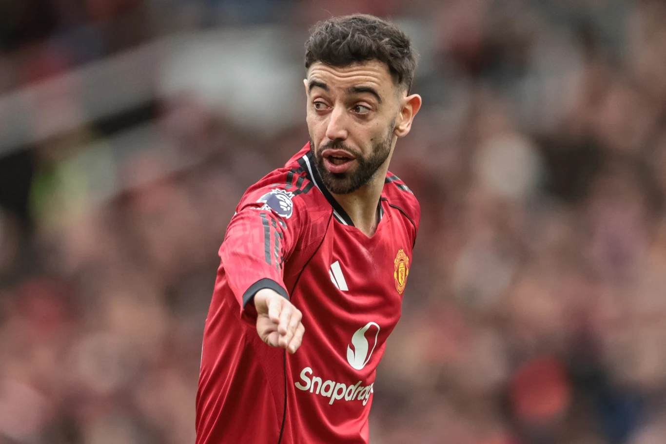 Bruno Fernandes piłkarz Manchesteru United w czerwonej koszulce z uniesioną ręką wskazującą kierunek, dynamiczny wyraz twarzy sugerujący komunikację z drużyną podczas meczu