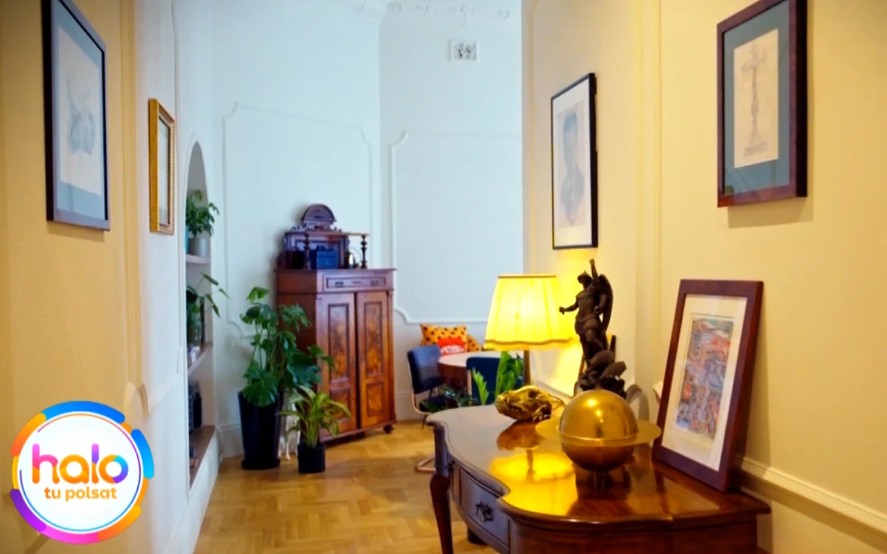 jasny, elegancki korytarz z drewnianą komodą, lampą stołową i dekoracjami, na ścianach wiszą obrazy, w tle widoczna zielona roślina i stylowy, drewniany kredens z dekoracjami