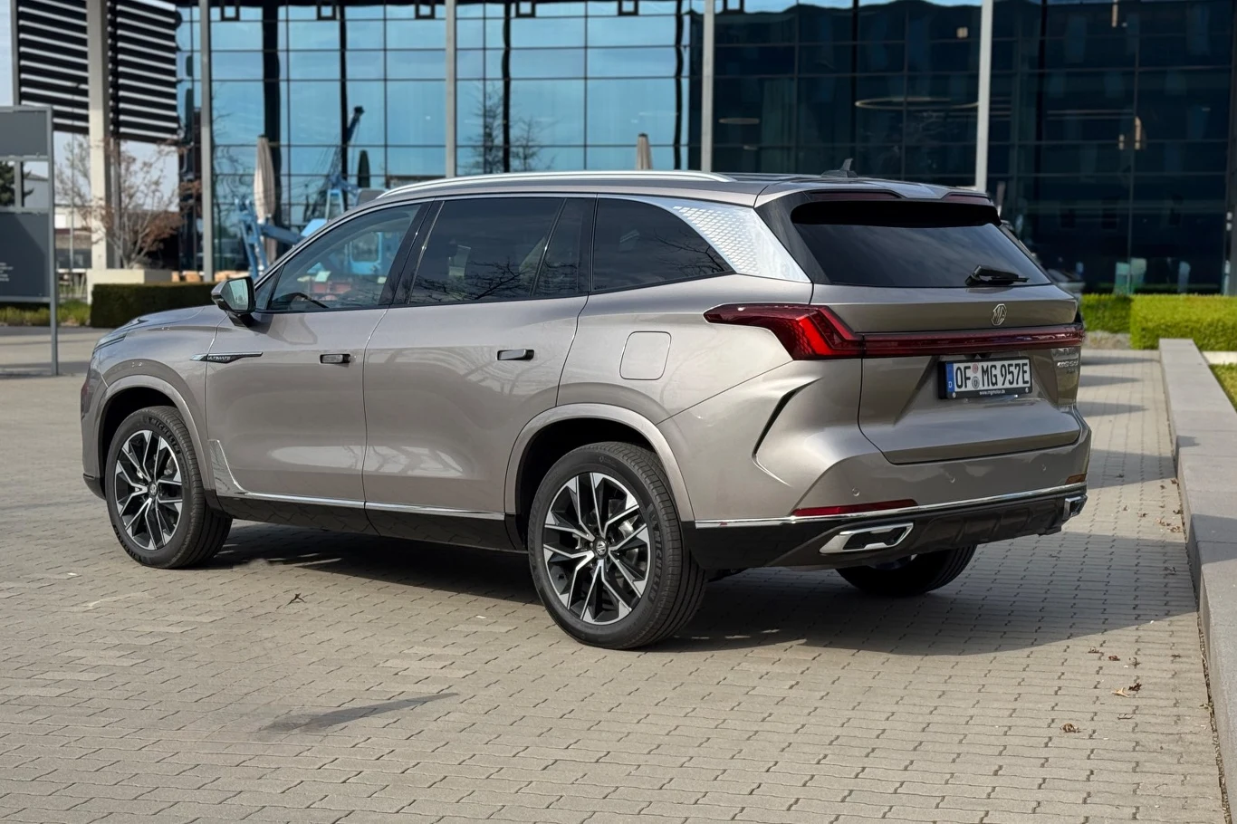 W stylizacji tylnej części można doszukać się podobieństw do Lexusa lub BMW szary nowoczesny SUV z przyciemnianymi szybami i eleganckimi felgami, zaparkowany na brukowanym placu przed szklanym budynkiem biurowym