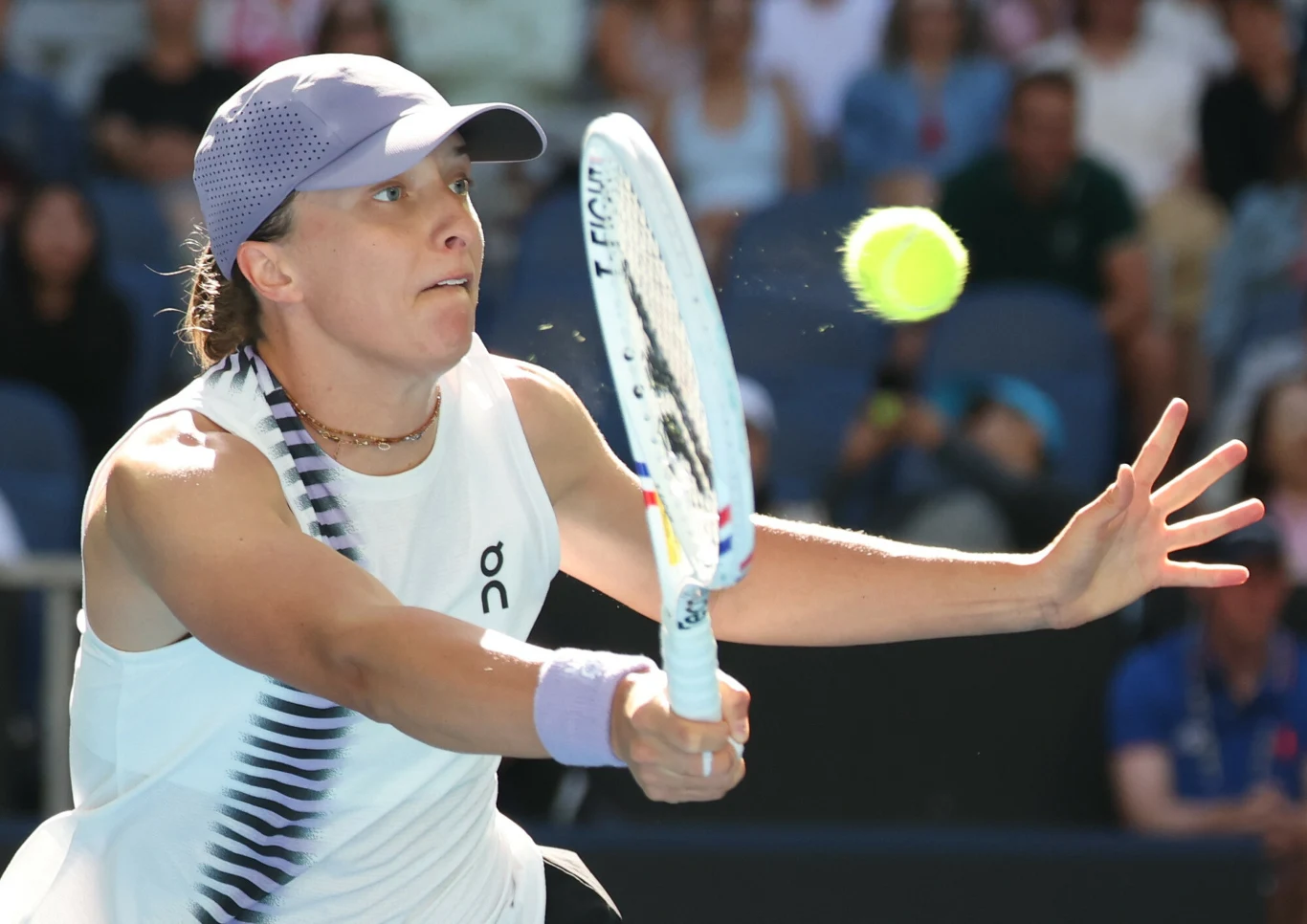 tenisistka w białym stroju i fioletowej czapce skupiona na odbiciu żółtej piłki tenisowej przy użyciu rakiety, dynamiczna akcja na tle rozmytej publiczności