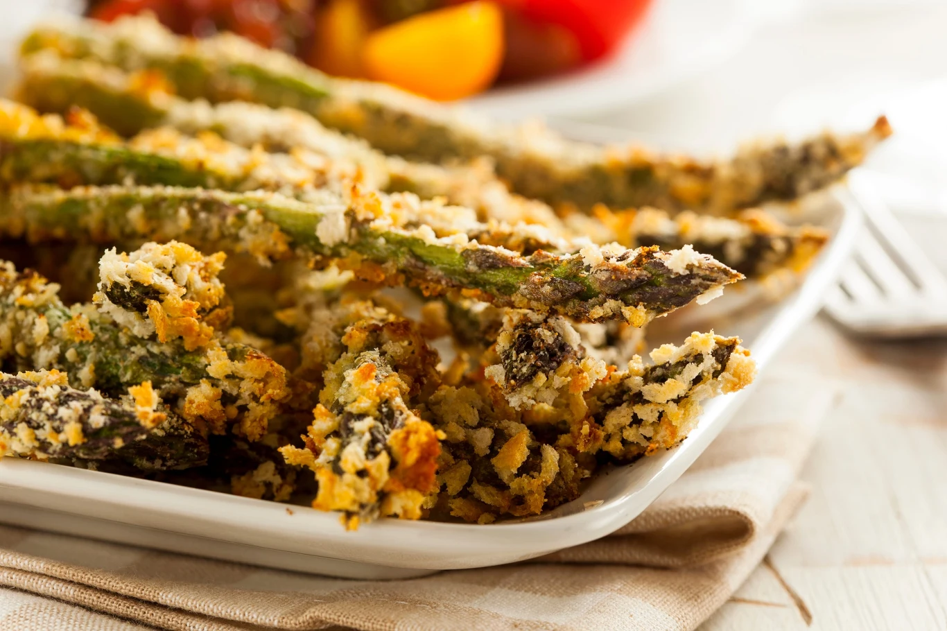 Szparagi w panierce zrumienione na złoto, ułożone na białym talerzu, z widocznymi chrupiącymi kawałkami panierki i apetyczną teksturą.