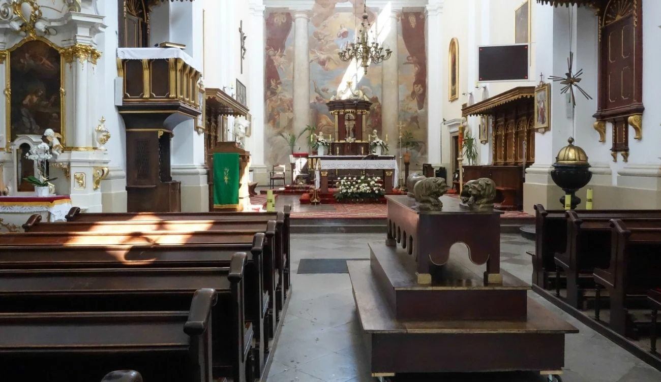 Wnętrze kościoła z drewnianymi ławkami, centralnym ołtarzem udekorowanym kwiatami i obrazami, amboną po lewej stronie oraz dużym sarkofagiem ustawionym przy głównym przejściu.