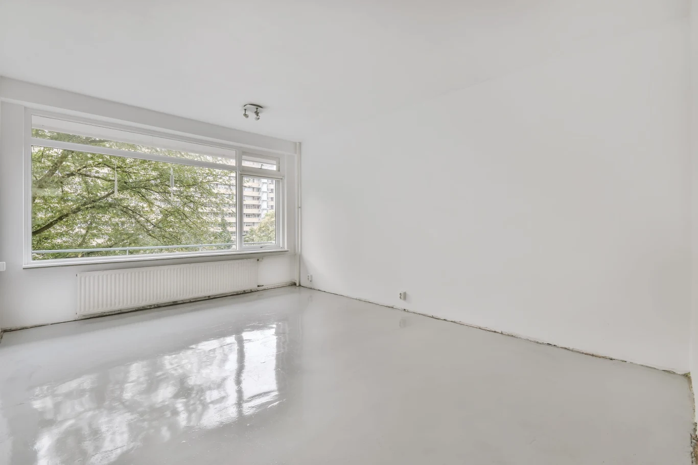 jasne, puste pomieszczenie z dużym oknem na ścianie, przez które widać drzewa i fragmenty budynków