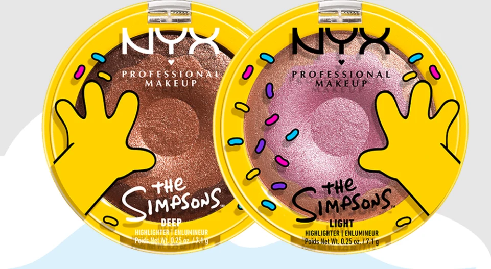 Tak wygląda nowa kolekcja NYX x The Simpsons Dwie okrągłe puderniczki marki NYX Professional Makeup w edycji The Simpsons, każda z żółtą ręką przypominającą postać z kreskówki i kolorowymi posypkami wokół wieczka, zawierające rozświetlacze w odcieniach głębokiego brązu i jasnoróżowego.
