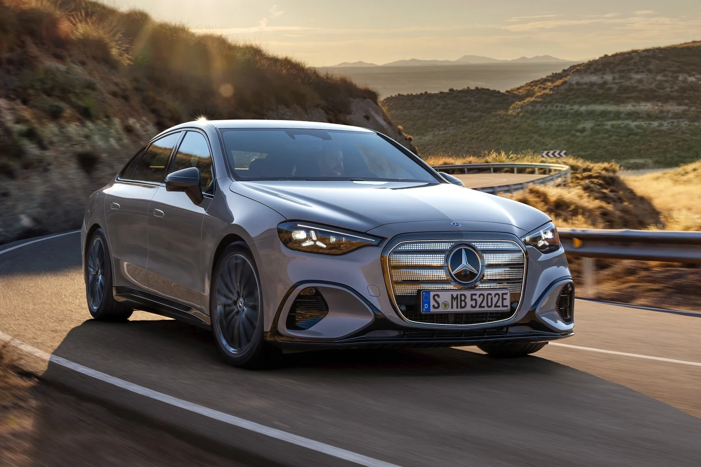 Mercedes klasy C electric Srebrny Mercedes-Benz klasy S z nowoczesnym, aerodynamicznym designem jedzie po krętej, asfaltowej drodze wśród malowniczych wzgórz o zachodzie słońca.