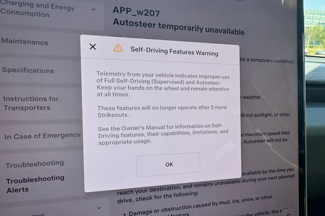 Komunikat ostrzegawczy na ekranie systemu pojazdu informujący o nieprawidłowym korzystaniu z trybu Full Self-Driving i Autosteer, z wyraźnym poleceniem trzymania rąk na kierownicy i zachowania czujności oraz informacją o możliwym wyłączeniu tych funkcj...