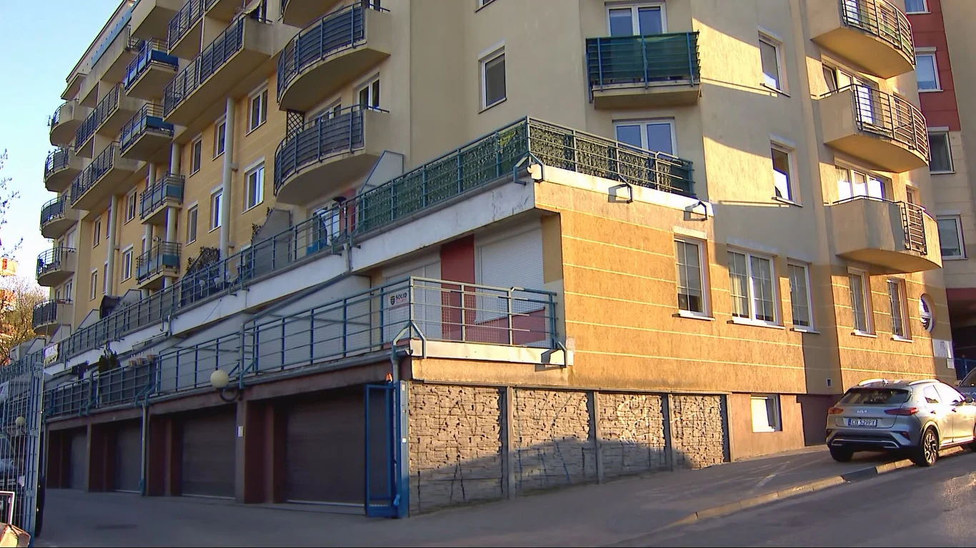 wielopiętrowy budynek mieszkalny z licznymi balkonami, garażami na parterze oraz zaparkowanym samochodem osobowym przy wjeździe