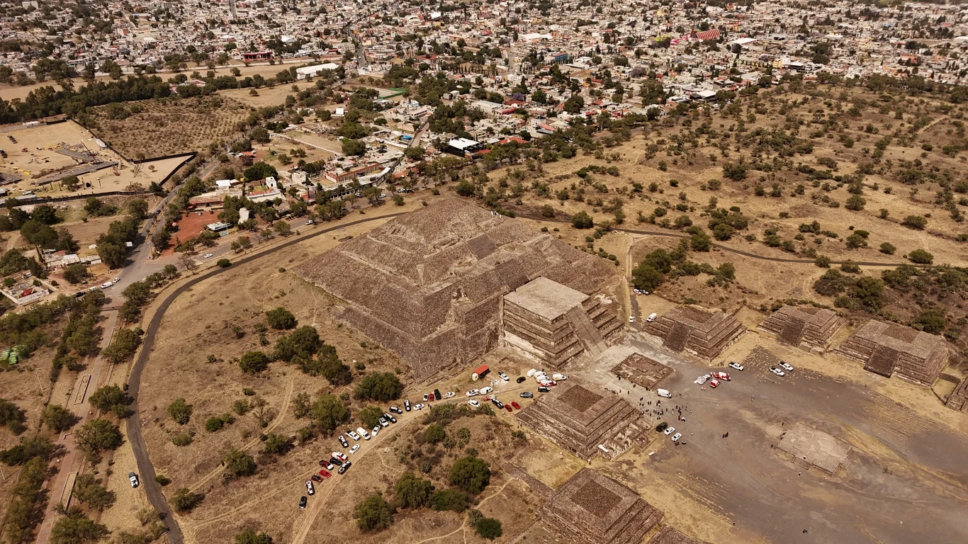 kompleks monumentalnych piramid i budowli archeologicznych wśród suchego terenu, otoczony drogą z zaparkowanymi samochodami, w tle widoczne gęsto zabudowane miasto
