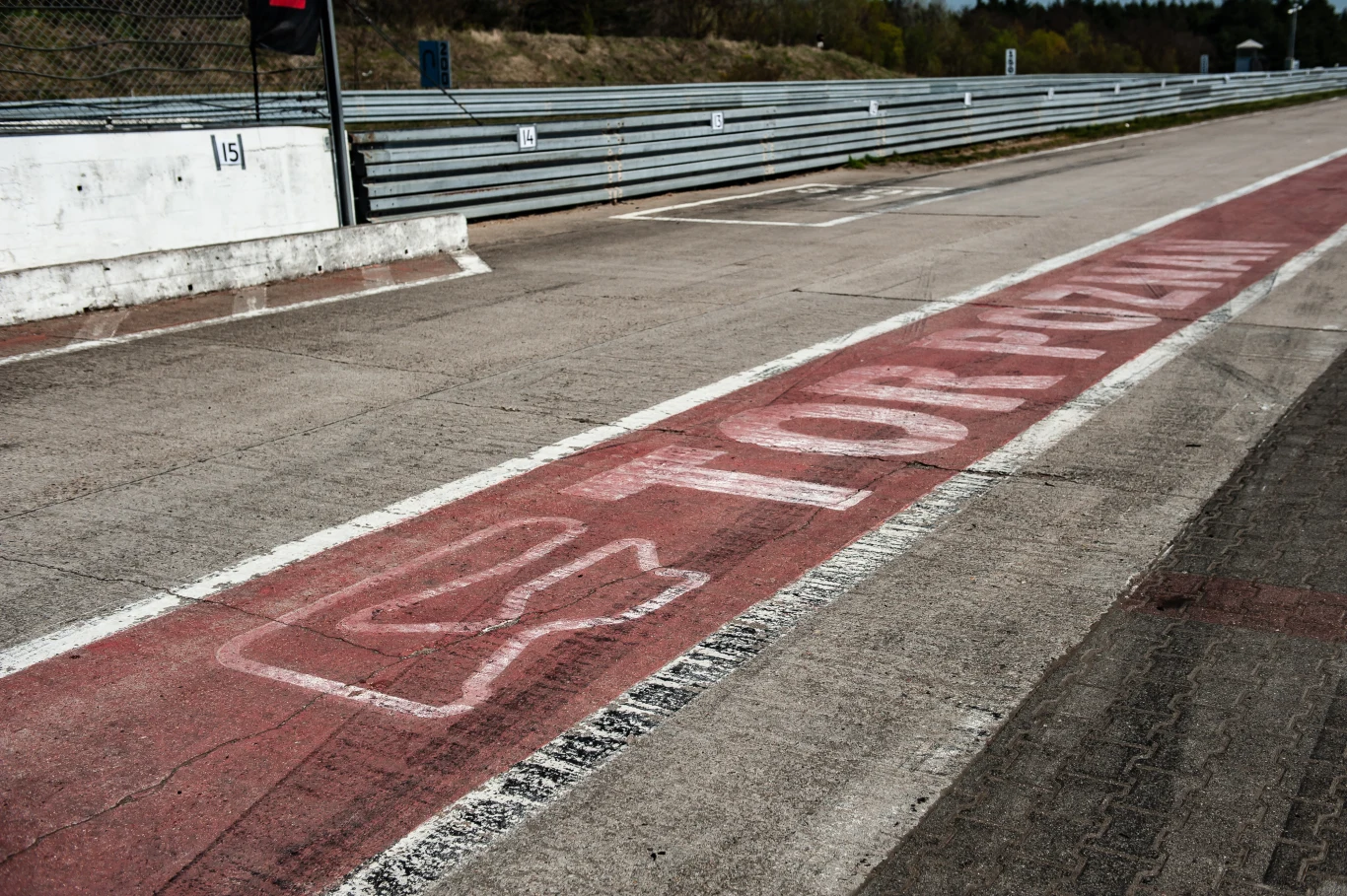 Trudno sobie nawet wyobrazić, by Tor Poznań zniknął z mapy Polski. To najlepszy taki obiekt w naszym kraju. | Fot. Toyota Gazoo Racing Polska asfaltowa nawierzchnia toru wyścigowego z wyraźnym czerwonym pasem oznaczonym napisem „Tor Poznań” oraz symbolicznym logo, metalowe barierki ochronne na tle lekkiego zagajnika