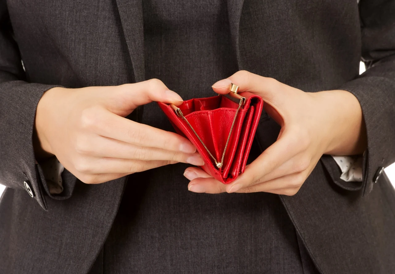 Osoba w garniturze trzyma pusty czerwony portfel, który jest szeroko otwarty.