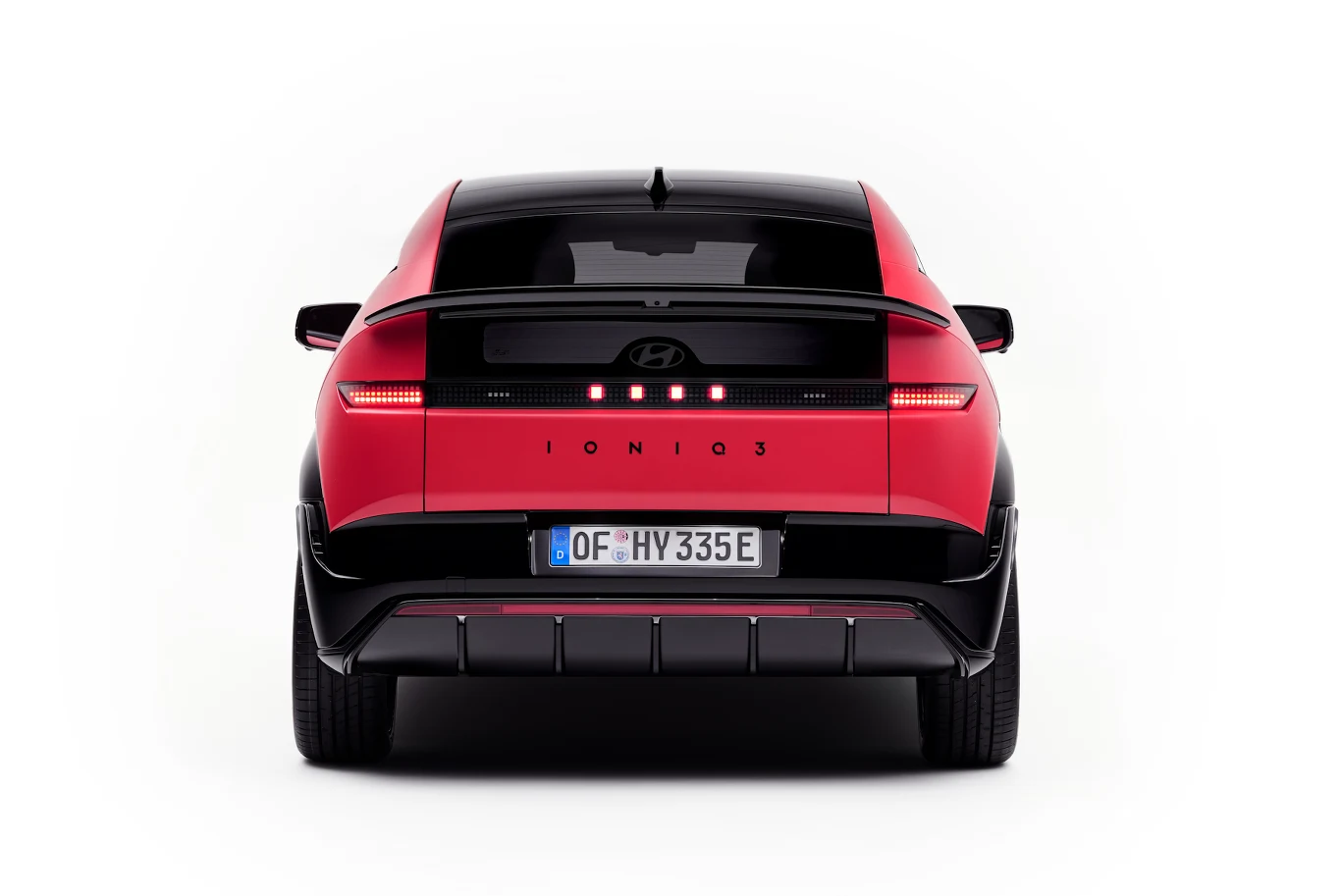 Hyundai Ioniq 3 Czerwony samochód Hyundai IONIQ 5 sfotografowany od tyłu, wyraziste światła LED, czarne elementy tylnej klapy i nowoczesny, aerodynamiczny zderzak, wyraźnie widoczna tablica rejestracyjna z napisem 'HY 335E'.