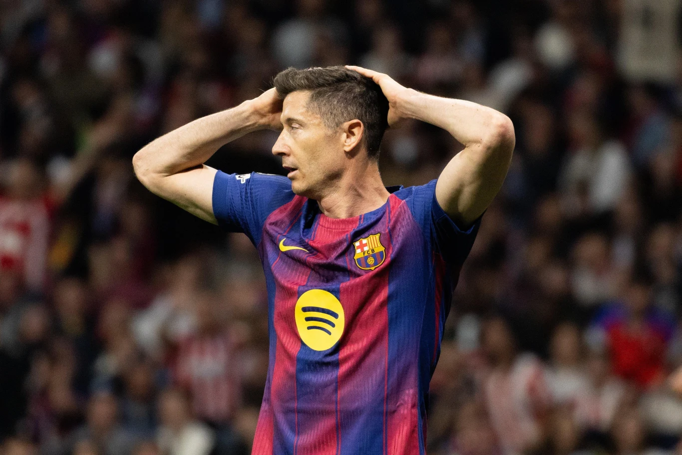Robert Lewandowski Robert Lewandowski w koszulce FC Barcelony z rękami na głowie; w tle rozmyty tłum kibiców.