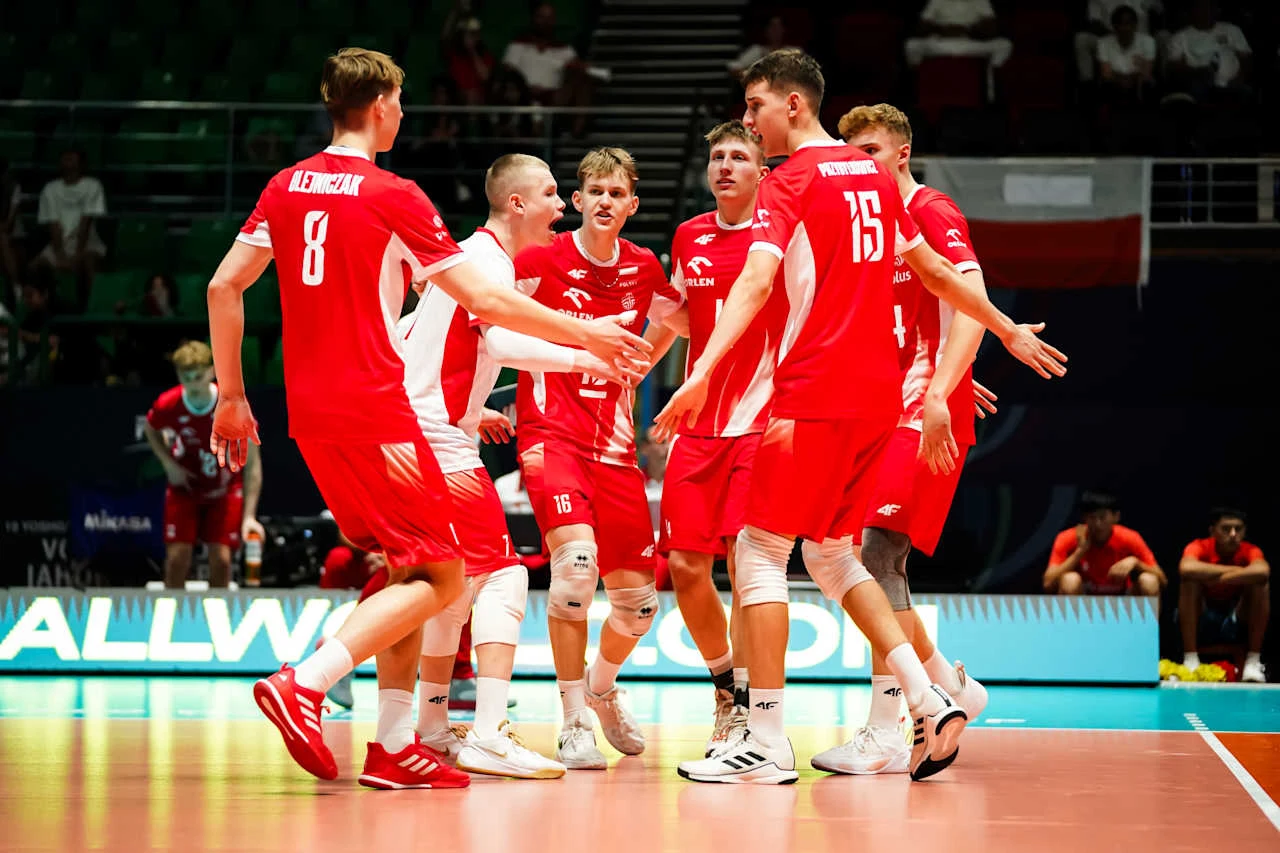 grupa młodych siatkarzy w czerwonych strojach świętuje udaną akcję na boisku, otoczona energiczną atmosferą sportowych zmagań, w tle widać polską flagę na trybunach