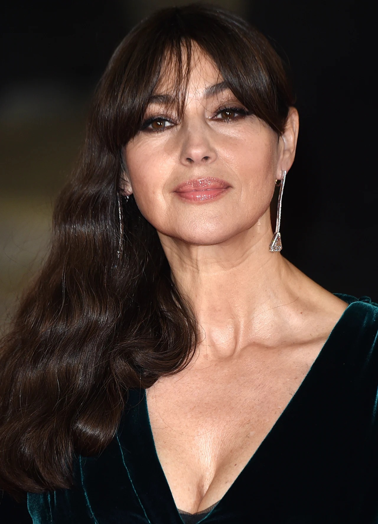 kobieta z długimi, ciemnymi włosami, w eleganckiej welurowej sukni z głębokim dekoltem, nosząca długie, srebrne kolczyki, o delikatnym makijażu i łagodnym wyrazie twarzy