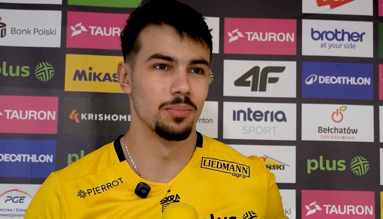 Daniel Chitigoi Młody mężczyzna w żółtej koszulce sportowej udziela wywiadu na tle tablicy z licznymi logotypami sponsorów i partnerów sportowych, trzymając mikrofon.