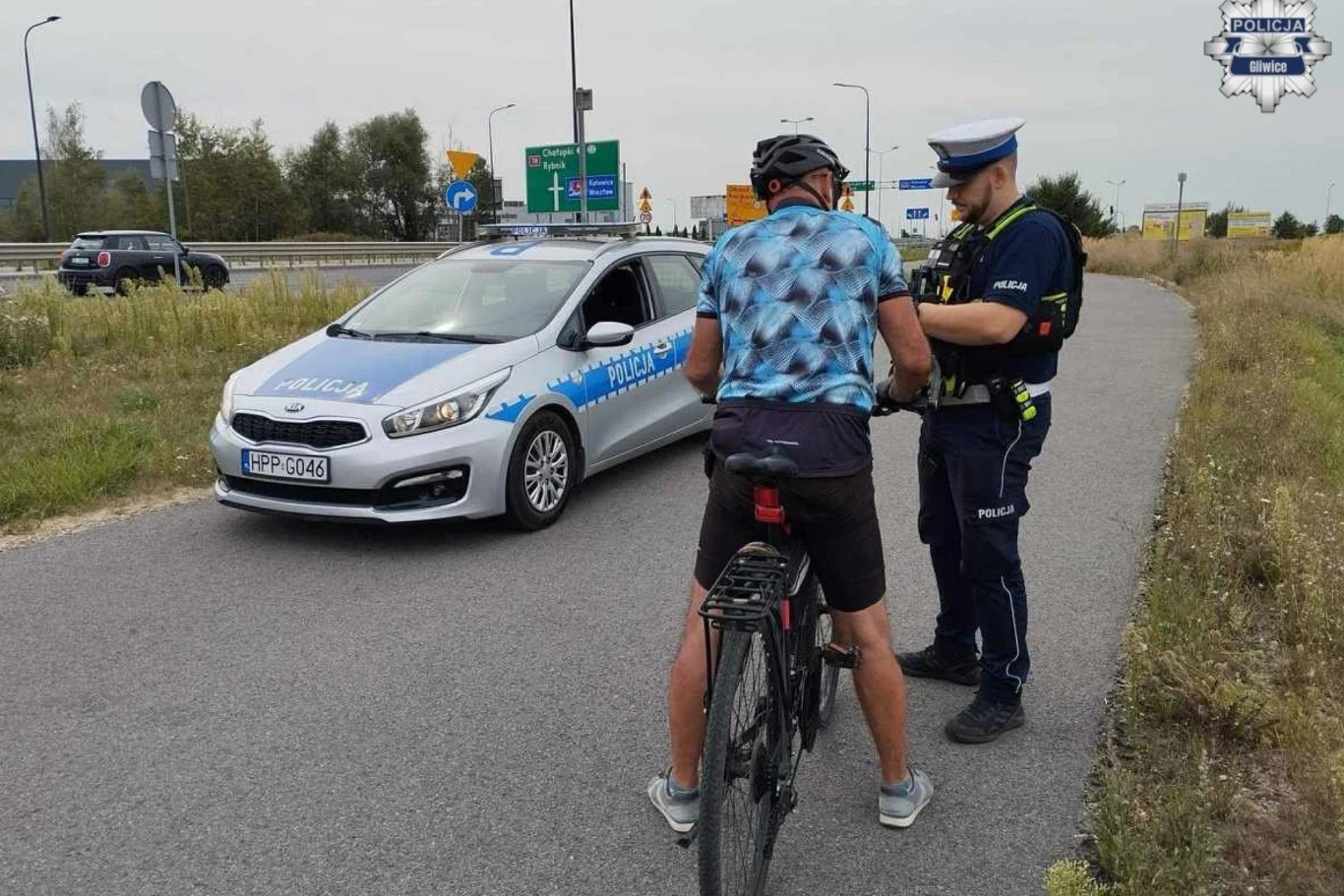 Policjanci mogą kontrolować trzeźwość rowerzystów. policjant w mundurze rozmawia z rowerzystą zatrzymanym na poboczu drogi, obok stoi radiowóz policyjny zaparkowany na asfalcie