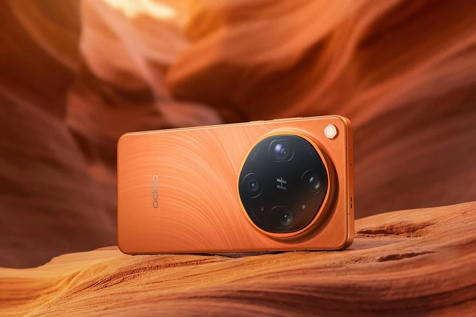 Oppo Find X9 Ultra w kolorze Canyon Orange. pomarańczowy smartfon z dużą okrągłą wyspą aparatów i srebrnym obramowaniem, położony na tle piaskowych skał o podobnym odcieniu