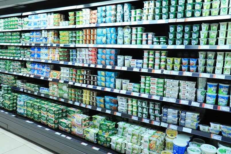 Danone Półki chłodnicze wypełnione różnorodnymi produktami nabiałowymi, głównie jogurtami, kefirami i serkami pakowanymi w plastikowe kubki i pojemniki, ułożonymi warstwami według marki oraz rodzaju, dominują jasne, kremowe i zielone etykiety.