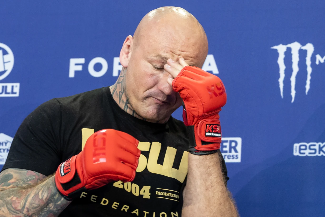 Artur Szpilka Artur Szpilka w czerwonych rękawicach, opierający dłoń o czoło na tle niebieskiej ścianki z logotypami sponsorów