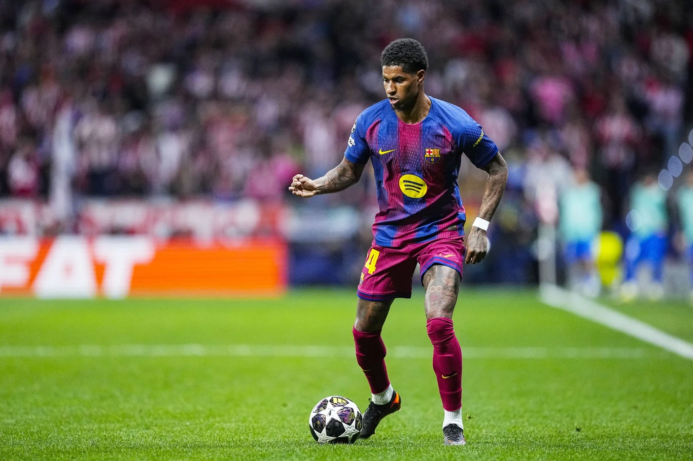 Marcus Rashford piłkarz w bordowo-granatowej koszulce z żółtym logo drybluje piłkę na boisku podczas meczu, w tle rozmazana publiczność na trybunach