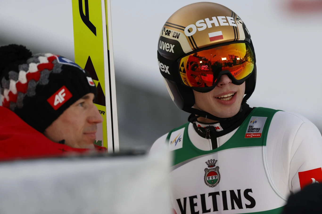 Kamil Stoch i Kacper Tomasiak Kamil Stoch i Kacper Tomasiak w kombinezonach skoczków, rozmowa z trenerem w polskiej czapce szachownicy