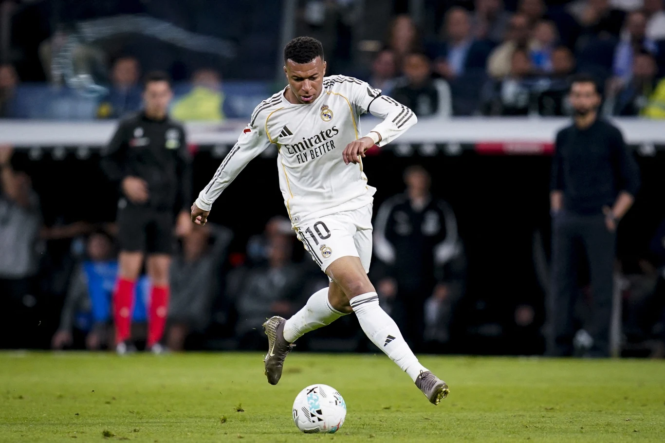 Kylian Mbappe w barwach Realu Madryt podczas meczu La Liga w sezonie 2025/2026 piłkarz Realu Madryt w białym stroju wykonujący dynamiczne podanie lub strzał na boisku podczas meczu, w tle rozmyta publiczność i sędziowie