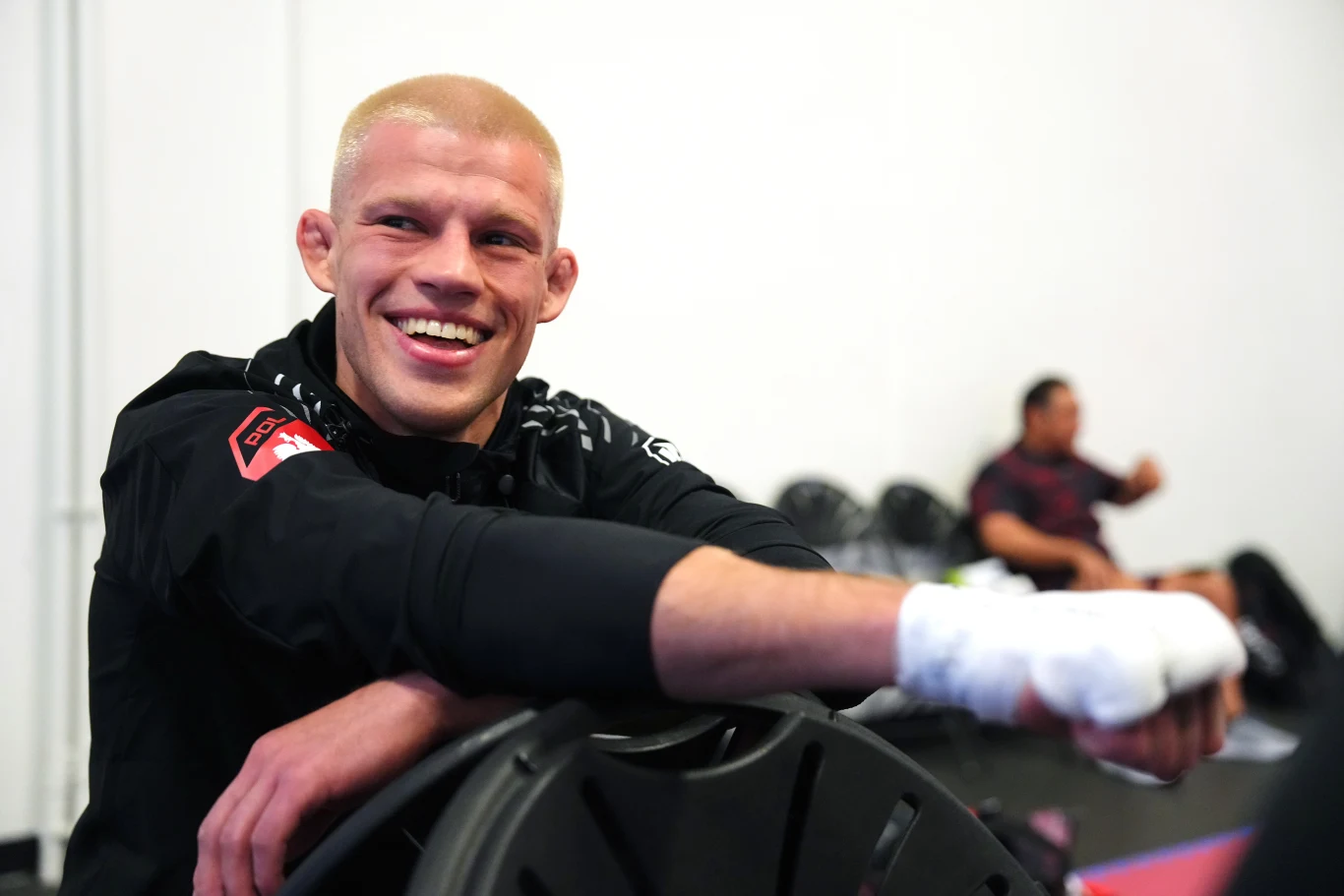 Jakub Wikłacz Jakub Wikłacz w sportowym stroju, oparty o krzesło z zabandażowaną dłonią; w tle ludzie i puste krzesła
