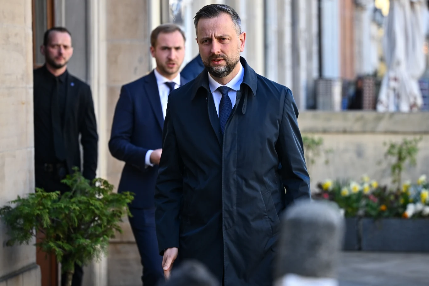 Szef MON Władysław Kosiniak-Kamysz o dostawach pocisków do amerykańskich systemów rakietowych: Jesteśmy w kontakcie ze stroną amerykańską i mamy informacje, że w niektórych obszarach mogą wystąpić opóźnienia Władysław Kosiniak-Kamysz w ciemnym płaszczu i niebieskim krawacie idzie chodnikiem, za nim dwaj mężczyźni w garniturach.