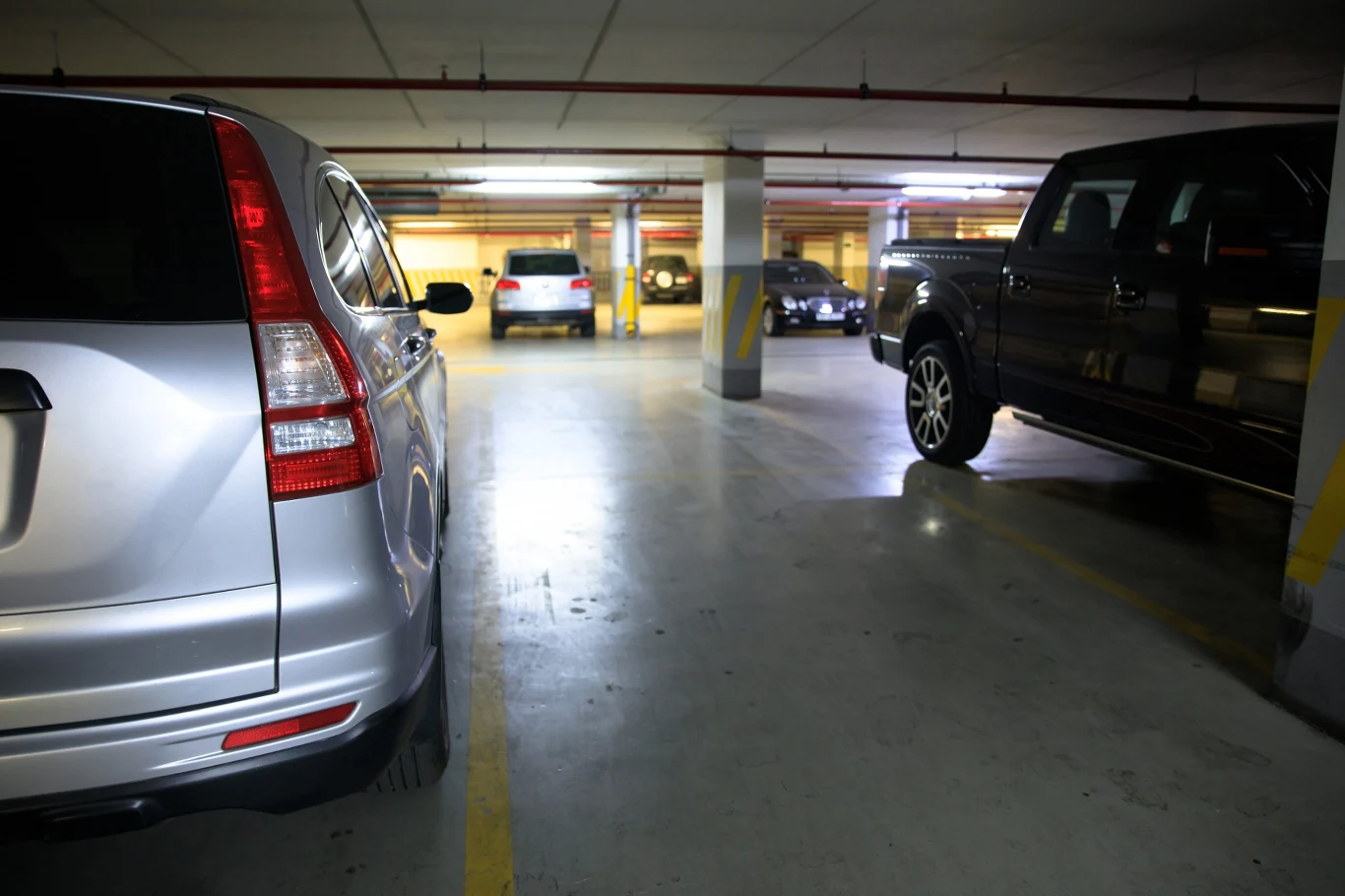 Stłuczka w garażu podziemnym. Przepisy, oświadczenie i policja. Podziemny parking z betonowymi filarami, zaparkowane auta, wyraźne linie miejsc parkingowych, dobre oświetlenie