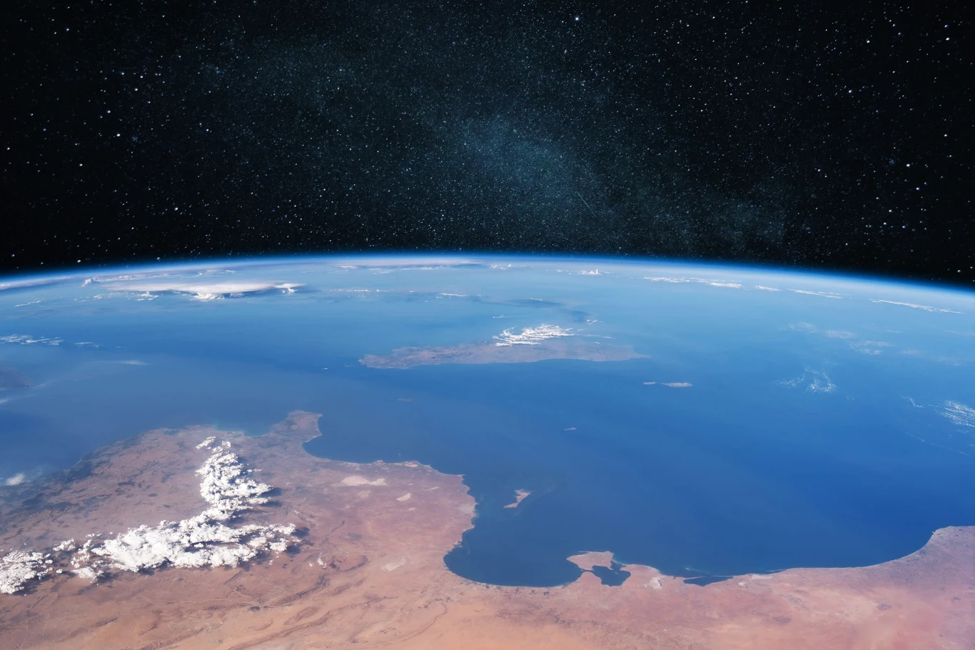 Miejsce położone najdalej od cywilizacji. Gdzie się znajduje? Krzywizna Ziemi widoczna z kosmosu, błękitna atmosfera, lądy, morza i ośnieżone góry na tle gwiazd.