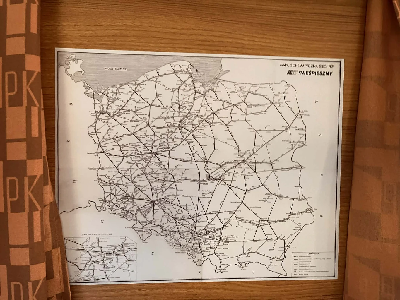 Na pokładzie Nieśpiesznego nawet mapa jest retro czarno-biała mapa Polski prezentująca szczegółową sieć linii kolejowych, umieszczona na tle drewnianej ściany i częściowo zasłonięta brązowymi zasłonami z powtarzającym się wzorem liter PKP