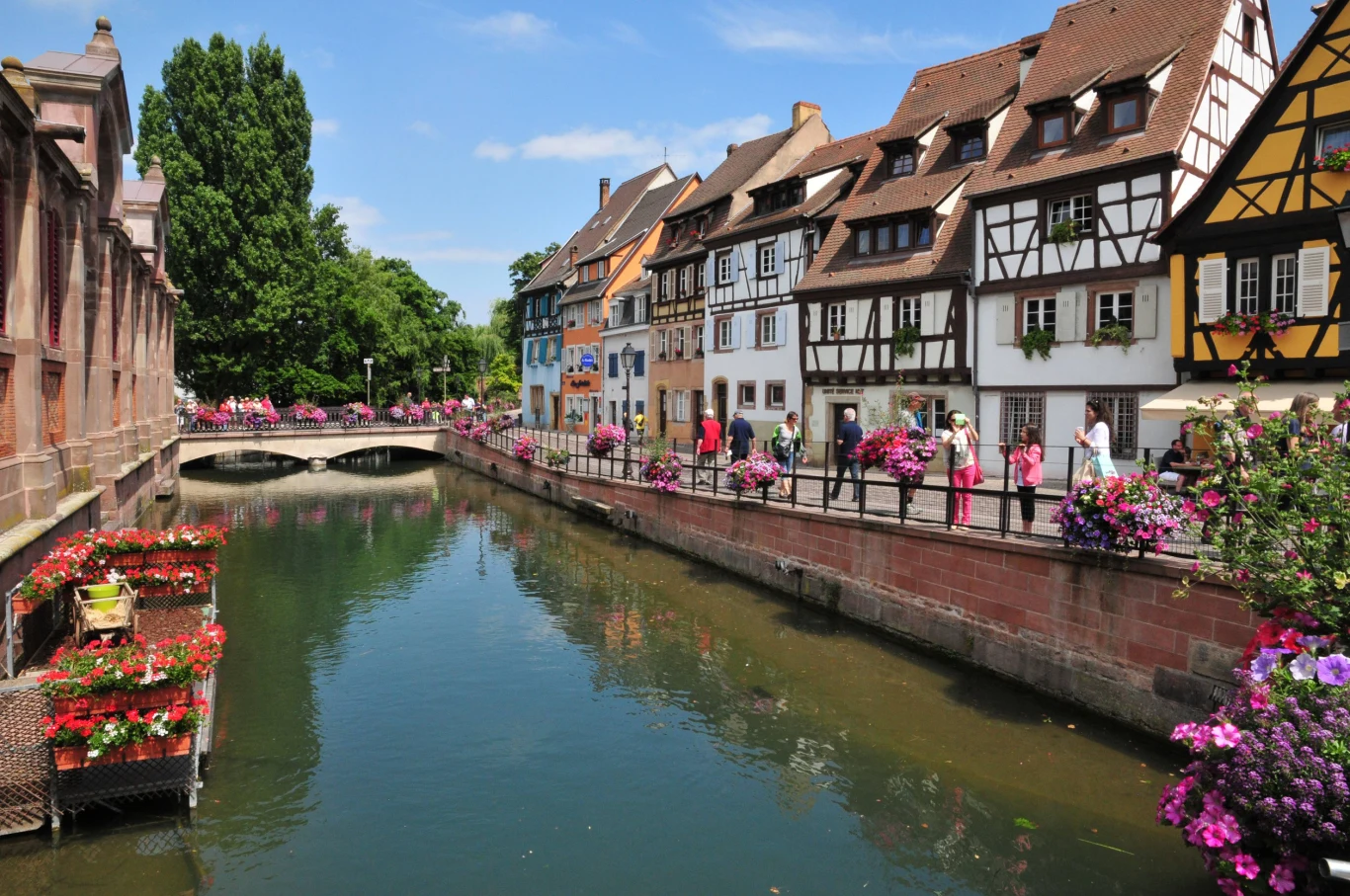 Najlepszym sposobem zwiedzania Colmar jest spokojny spacer Colmar: kolorowe kamienice z muru pruskiego i kwiatami nad rzeką, mostek i spacerujące osoby